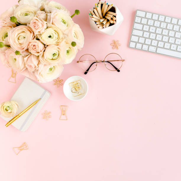 istock Stylized, pink women's home office desk. Workspace with computer, bouquet ranunculus and roses, clipboard on pink background. Flat lay. Top view 1276131708