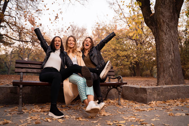 istock Three girls on park bench laughing with hands in air 1276134056