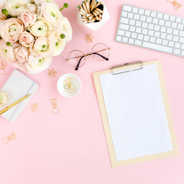 istock Stylized, pink women's home office desk. Workspace with computer, bouquet ranunculus and roses, clipboard on pink background. Flat lay. Top view 1276140098