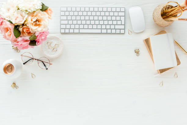 istock Flat lay women's office desk. Female workspace with computer, pink roses flowers, accessories, golden diary, glasses on white background. Top view 1276149587