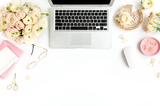 istock Stylized women's home office desk. Workspace with laptop, computer, bouquet ranunculus and roses, clipboard on white background. Flat lay. Top view 1276150603