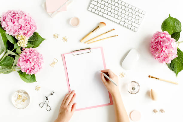 istock Female workspace with female hands, clipboard, bouquet hydrangea, computer, accessories on white background. Stylized women's desk. Flat lay. Top view 1276161589