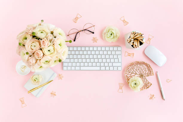 istock Stylized, pink women's home office desk. Workspace with computer, bouquet ranunculus and roses, clipboard on pink background. Flat lay. Top view 1276166897