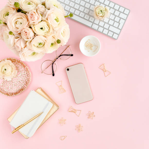 istock Stylized, pink women's home office desk. Workspace with computer, bouquet ranunculus and roses, phone on pink background. Flat lay. Top view 1276174926
