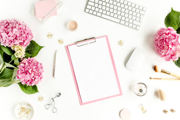 istock Stylized women's desk. Workspace with clipboard, computer, bouquet hydrangea, accessories on white background. Flat lay. Top view 1276176626