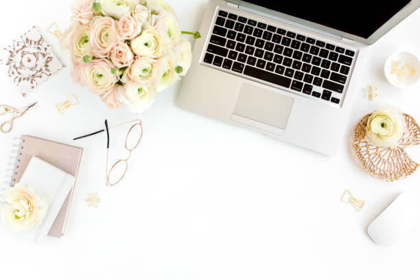 istock Stylized women's home office desk. Workspace with laptop, computer, bouquet ranunculus and roses, clipboard on white background. Flat lay. Top view 1276188300