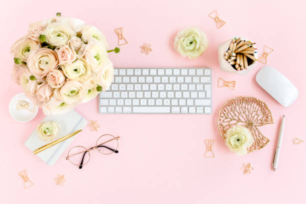 istock Stylized, pink women's home office desk. Workspace with computer, bouquet ranunculus and roses, clipboard on pink background. Flat lay. Top view 1276188889