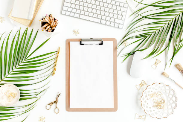 istock Flat lay home office desk. Female workspace with computer, clipboard, tropical palm leaves, accessories on white background. Top view 1276189021
