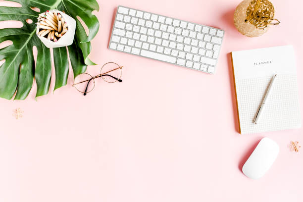 Flat lay home office desk. Female workspace with computer, tropical palm leaves Monstera, accessories on pink background. Top view background