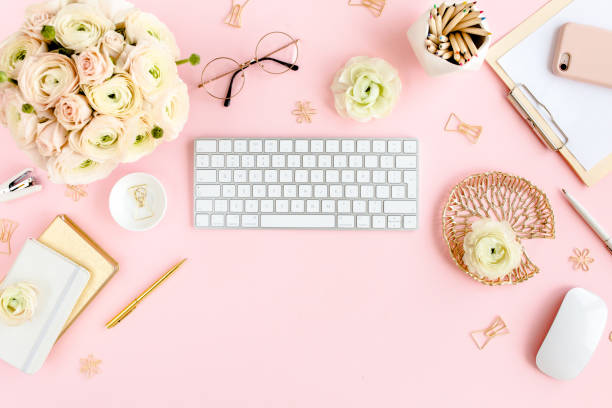 istock Stylized, pink women's home office desk. Workspace with computer, bouquet ranunculus and roses, clipboard on pink background. Flat lay. Top view 1276190125