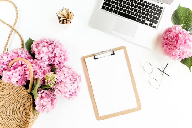 istock Stylized women's desk. Workspace with clipboard, laptop, bouquet hydrangea, accessories on white background. Flat lay. Top view 1276195103
