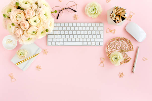 istock Stylized, pink women's home office desk. Workspace with computer, bouquet ranunculus and roses, clipboard on pink background. Flat lay. Top view 1276200737