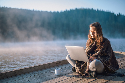Beautiful woman using laptop and drinking coffee in nature.