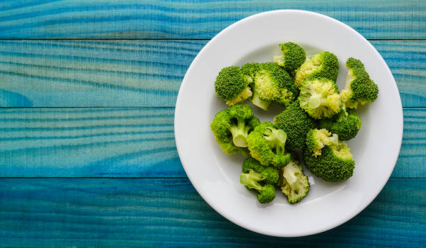 istock Fresh steamed Broccoli on a white ceramic plate on a vivid abstract blue/turquoise colored weathered wooden rustic table background. 1276354526