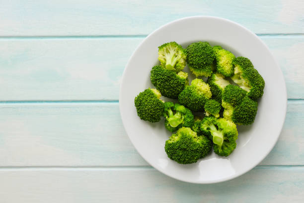 istock Fresh steamed Broccoli on a white ceramic plate on a light blue/turquoise colored weathered wooden rustic table background. 1276354532