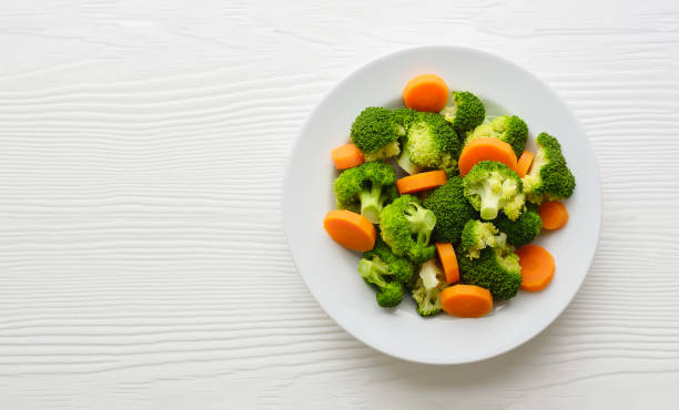 istock Fresh steamed broccoli and carrot on a white ceramic plate on a white colored wood table background. 1276355222