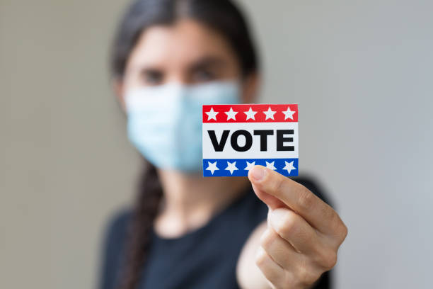 istock Young woman wearing face mask holding Vote sticker 1276356933