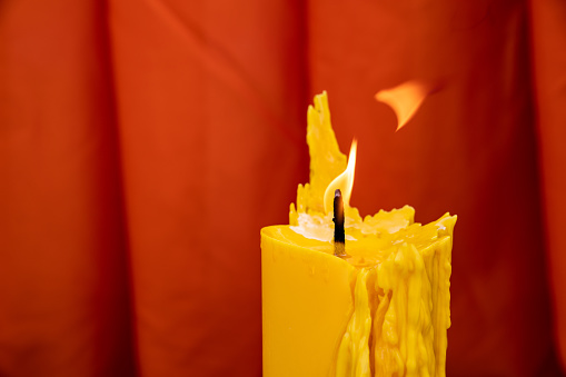 Close up to the melt yellow candle and fire flame with the red curtain background.