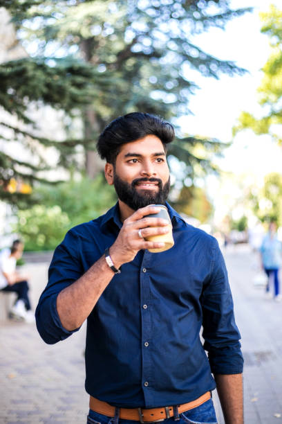 istock Young Indian man drinking coffee from reusable cup outdoors. 1276364122