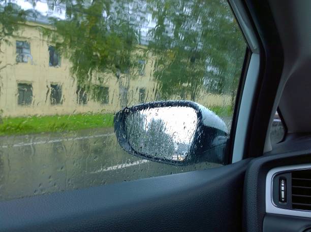image abstraite floue de la rue de ville à travers le verre d’automobile avec des gouttes de pluie. temps pluvieux et couvert. paysage urbain par la fenêtre du véhicule. des gouttes d’eau. miroir latéral humide de la voiture. pluies diluviennes - mirror reflection blues glass photos et images de collection