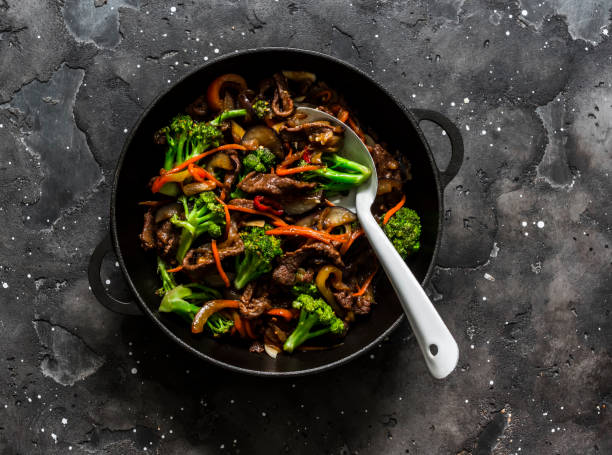 istock Fried beef with broccoli, carrots and chili peppers in a cast-iron pan on a dark background, top view 1276367625