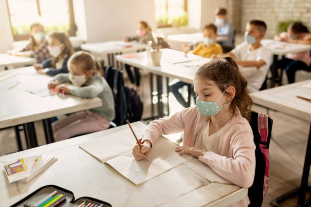 istock Little girl wearing face mask while learning with her classmates in the classroom. 1276371912