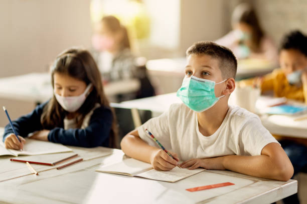istock Elementary student with face mask raising hands to answer a question in the classroom. 1276372626