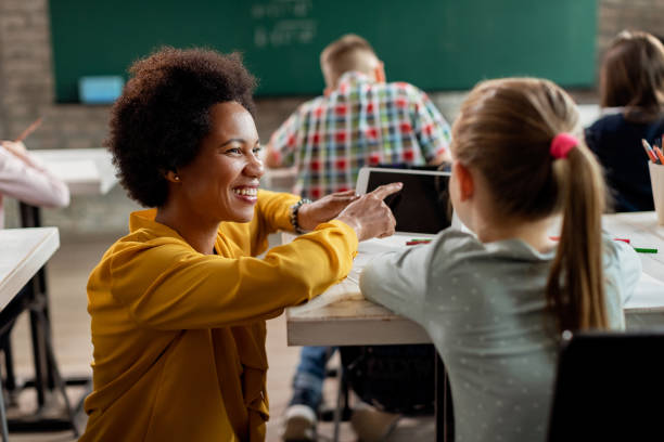 Happy black teacher and schoolgirl using digital tablet in the classroom. Happy African American teacher and elementary student using touchpad during a class in the classroom. elementary school building photos stock pictures, royalty-free photos & images