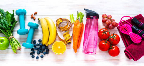 Exercising and healthy food: raibow colored fruits, vegetables and fitness items Exercising and healthy eating concept: overhead view of rainbow colored dumbbells, jump rope, water bottle, towel, tape measure and healthy fresh organic vegetables, fruits and nuts arranged side by side on white background. The composition includes spinach, tomato, carrot, banana, apple, blueberry, almonds, orange, celery, grape among others. High resolution 29Mp panoramic format studio digital capture taken with SONY A7rII and Zeiss Batis 40mm F2.0 CF lens exercise equipment photos stock pictures, royalty-free photos & images