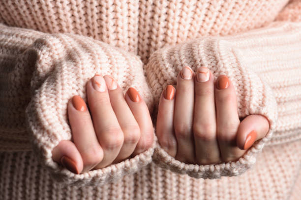 Female hands with trendy autumn marble manicure in orange color. Female hands with trendy autumn marble manicure in orange color. Pink knitted wool sweater fingernail stock pictures, royalty-free photos & images