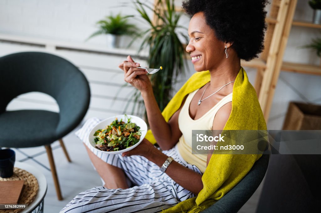 Beautiful afro american woman eating vegetable salad at home. Cheerful afro american woman eating fresh vegetable salad at home. Eating Stock Photo