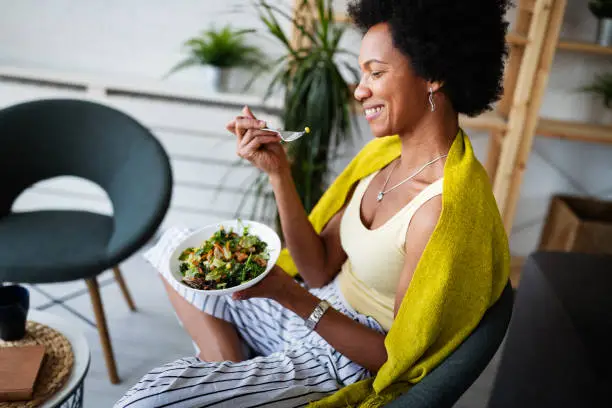 Photo of Beautiful afro american woman eating vegetable salad at home.