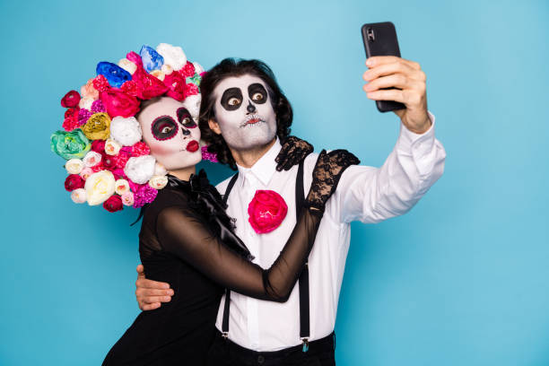 Photo of cute funny zombie couple man lady girl embrace hold telephone make selfie translate festival wear black dress death costume roses headband suspenders isolated blue color background Photo of cute funny zombie couple man lady girl embrace hold telephone, make selfie translate festival wear black dress death costume roses headband suspenders isolated blue color background carnival costume stock pictures, royalty-free photos & images