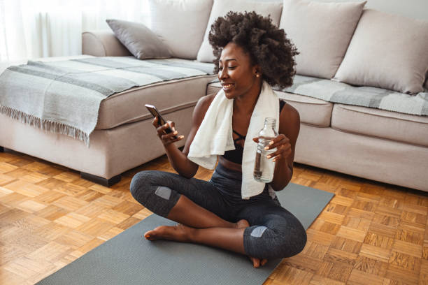 femme utilisant le téléphone intelligent sur le tapis d’exercice - bikram yoga pilates beautiful photos et images de collection