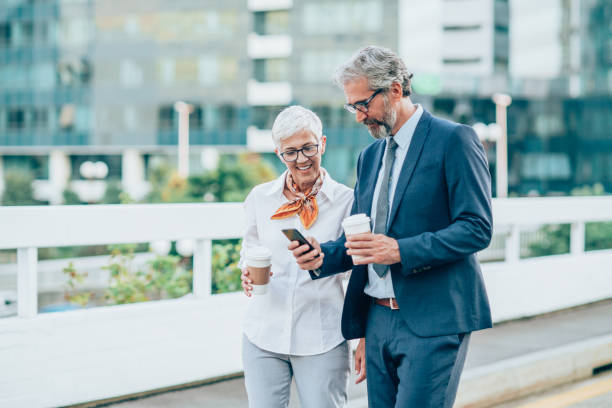 Two mature business persons using phone outdoors.