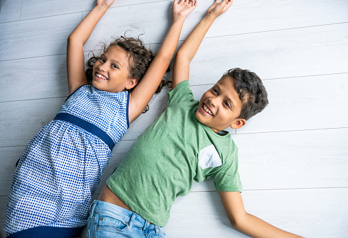 Two smiling mixed race children lying on the floor and smiling.