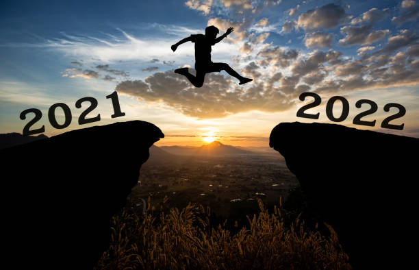 un joven salta entre 2021 y 2022 años sobre el sol y a través de la brecha de la silueta de la colina cielo colorido de la noche. feliz año nuevo 2021. - intend fotografías e imágenes de stock