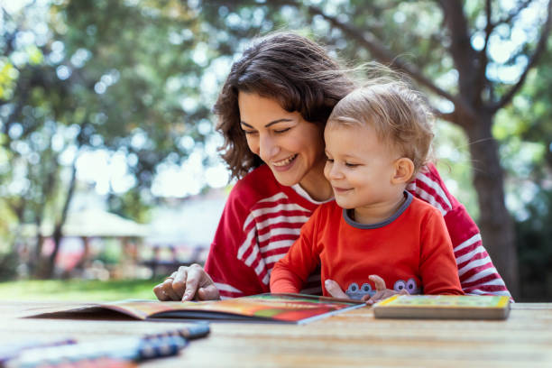 madre e figlio che leggono libri al giardino, con pastelli sul tavolo da picnic - baby mother summer park foto e immagini stock