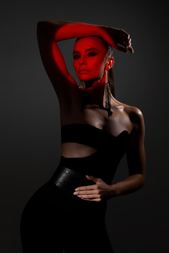 portrait of beautiful sexy brunette woman looking at the camera on dark background. red color light