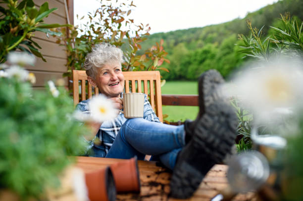 donna anziana con caffè seduto sulla terrazza in estate, a riposo. - balcony women patio coffee foto e immagini stock