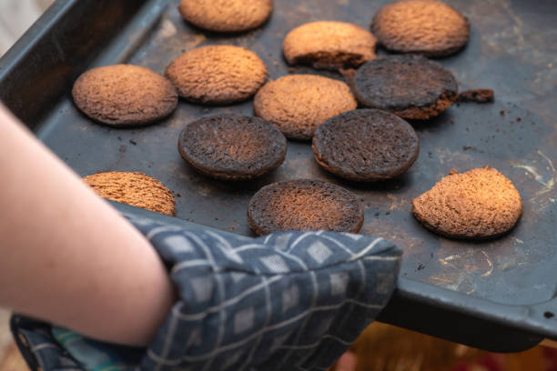 biscuits brûlés. une main dans un gant de four, potholder ramasse une plaque à pâtisserie noire avec des biscuits brûlés - cooking fail photos et images de collection