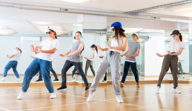 Group of teenagers in casual clothes training hip-hop in class, learning modern dance movements