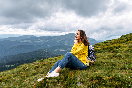 Side view of girl hiker with a backpack in summer mountains. A woman is enjoying scenic landscape and relaxing