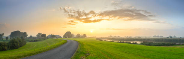 Sunrise over the IJsseldelta landscape near Kampen in Overijssel Sunrise over the IJsseldelta near Kampen in Overijssel. The road on the levee between Kampen and Zwolle is winding into the distance where old farms are situated on the side of the dyke. Wide panoramic photo ijssel photos stock pictures, royalty-free photos & images