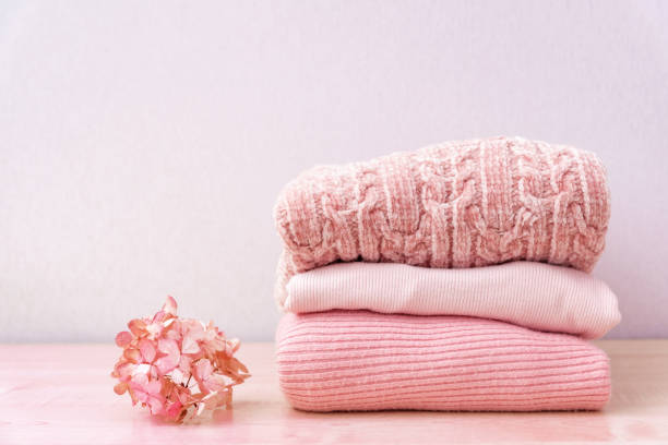 Stack of folded wool knitted sweaters in pink pastel colors laying on table for autumn winter season with flower Stack of folded wool knitted sweaters or pullovers in pink pastel colors on table with flower hydrangea. Close up of warm cozy comfortable monochrome clothes for autumn winter season. monochrome clothing stock pictures, royalty-free photos & images