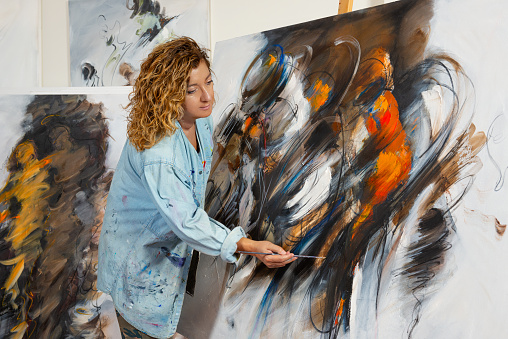 Fine art painter works in her studio, Painted canvases surrounds her.