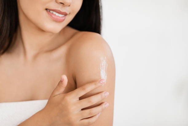istock Young asian lady wrapped in towel moisturizing her skin 1276412603