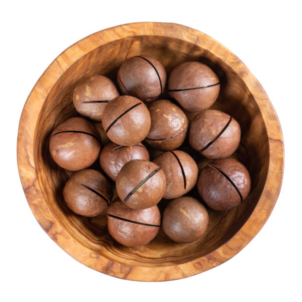 istock Macadamia nuts in wooden bowl isolated on white. Top view. 1276412756