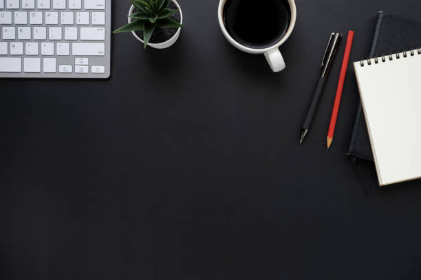 istock Top view above of Black office desk table with keyboard, notebook and coffee cup with equipment other office supplies. Business and finance concept. Workplace, Flat lay with blank copy space. 1276421926