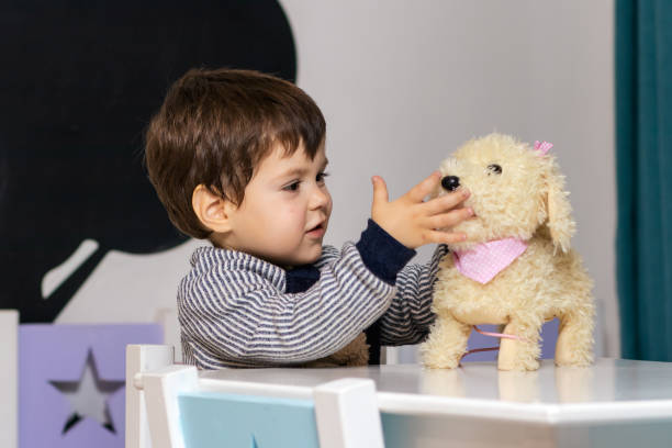 A little boy plays with a plush dog sitting at a table.